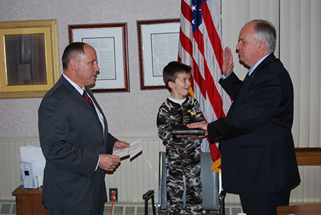 Islandia Village Attorney Joseph Prokop (left) swears in Village Mayor (right) at the April 2 Village Board meeting, with the Bible being held by Collin (center), Mayor Dorman's grandson.