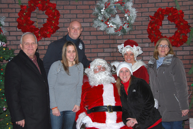 Islandia Village Mayor Allan M. Dorman (left) is joined by Santa Claus (center, seated) and Village Trustees and staff members at the 12th Annual Christmas Tree Lighting on December 2. He is joined by (left to right) Denise Schrage, Village Activities Director; Carrie Hays, Ms. Schrage’s sister; “Mrs. Claus” Barbara Lacey, and Patty Peters, Village Trustees. Standing behind Ms. Schrage: Michael Zaleski, Deputy Mayor.