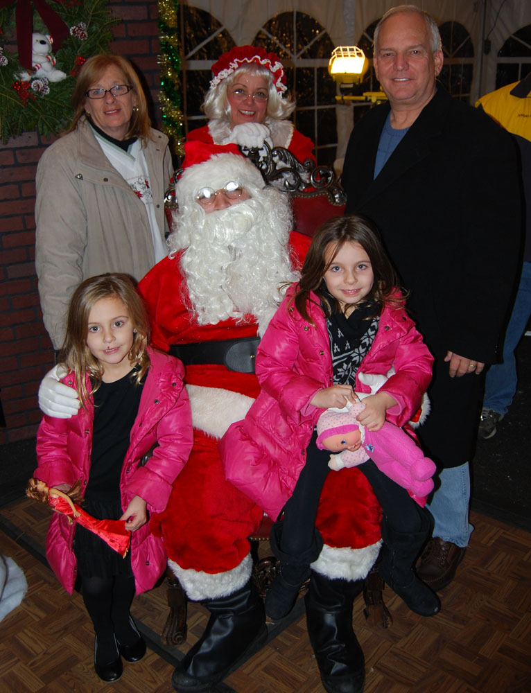 Islandia Village Trustees Patricia Peters (back row, left) and Barbara Lacey as “Mrs. Claus” (back row, center) and Mayor Allan Dorman (back row, right) pose with Santa Claus at the village’s 6th annual Christmas tree lighting ceremony. They are also joined by Abigail and Holly Neri, whose family helped light the tree.