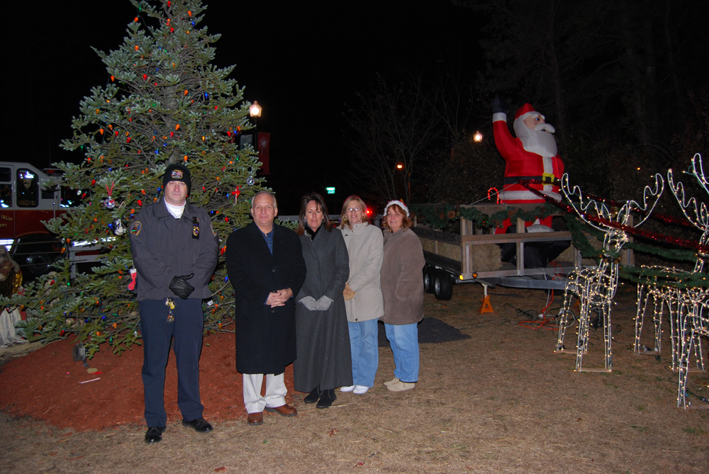 Islandia Village Mayor Allan Dorman (second from left) and Deputy Mayor Diane Olk (center) pose in front of the village’s Christmas tree after the tree lighting ceremony.