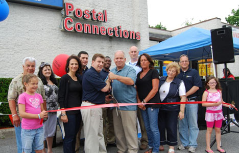 Standing behind the ribbon (left to right): Tony Church, Highway Commissioner, and Audrey Giordano; Teresa Colabella, Co-Owner, Eric Molina, Assistant Manager, Louis Colabella, Co-Owner and Raisson Elliott, Assistant Manager, Postal Connections; Allan M. Dorman, Mayor; Mike Zaleski, Trustee; Diane Olk, Deputy Mayor; Jerri Bixon, Broker, Brown Harris Stevens; Ralph Fiorillo, Manager, Postal Connections. Holding the ribbon are Mr. Fiorillo's daughters, Christie Snyder (left) and Jeanna Fiorillo (right).