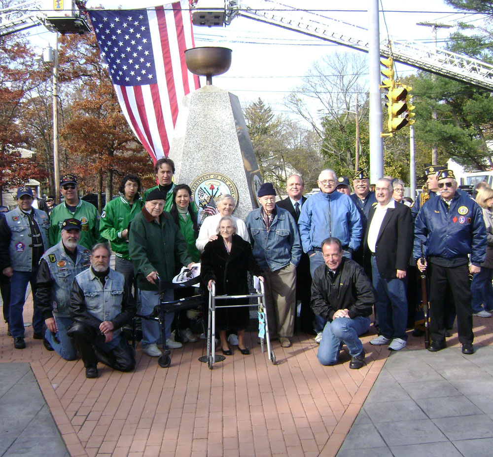 Islandia Village Mayor Allan Dorman (fifth from right) poses with local war veterans and residents from The Arbors Assisted Living in front of the Islandia Village War Veterans Memorial.